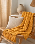 Fringed Diamond Knit Cotton Throw in Mustard, on a rattan armchair